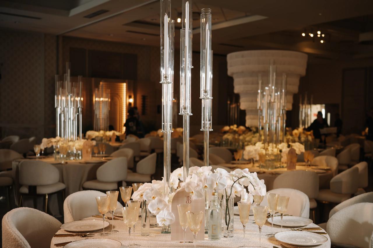 Warm indoor reception tablescape with white orchids and tall glass candle centerpiece arrangements on round tables. Bar Mitzvah photography at Hilton Garden Inn Springfield, Springfield, NJ.