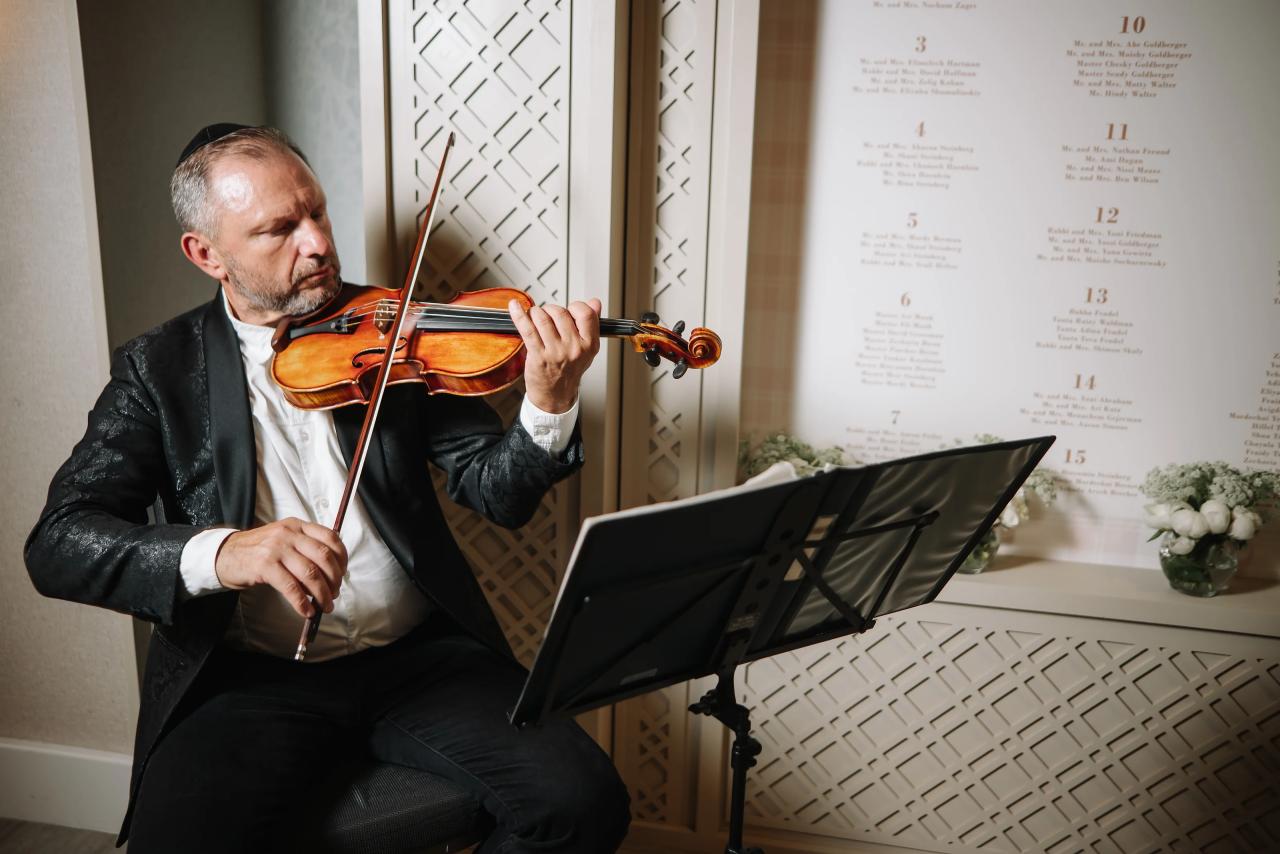 A violinist in formalwear performs beside a music stand at the bar mitzvah reception. Bar Mitzvah photography at Hilton Garden Inn Springfield, Springfield, NJ.