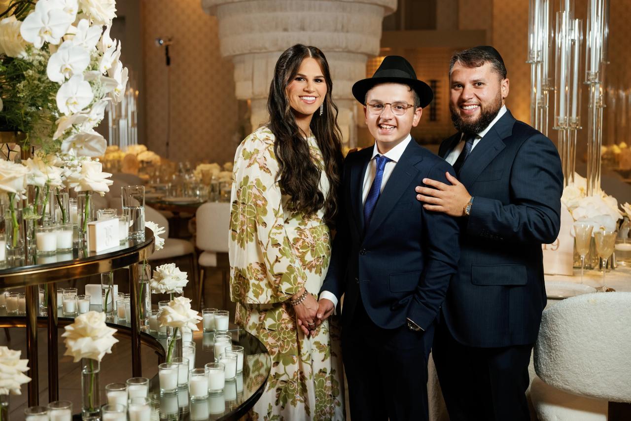 Family members pose together at the bar mitzvah reception beside a decorated sweets table with candles and flowers. Bar Mitzvah photography at Hilton Garden Inn Springfield, Springfield, NJ.