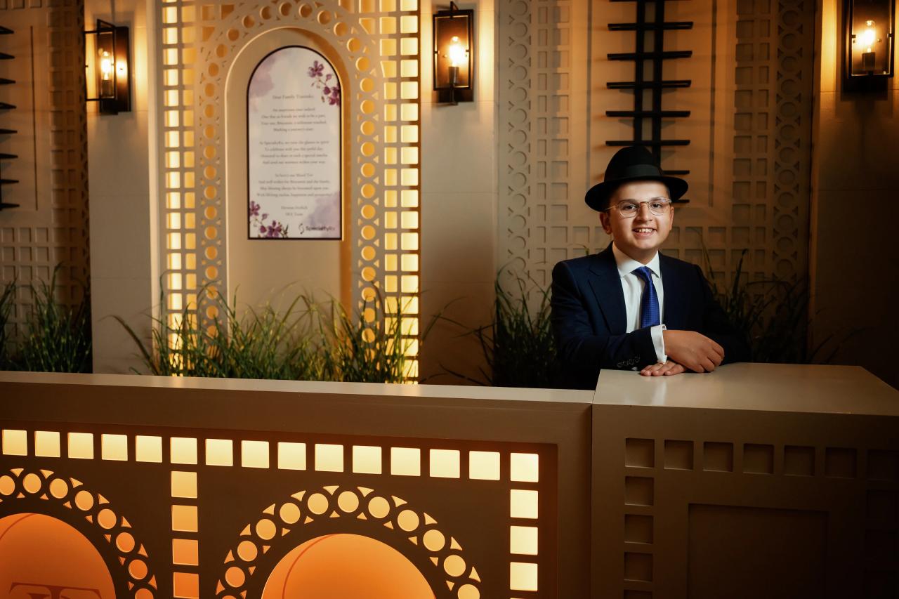 The bar mitzvah boy framed by a decorative wooden partition and warm wall lighting. Bar Mitzvah photography at Hilton Garden Inn Springfield, Springfield, NJ.