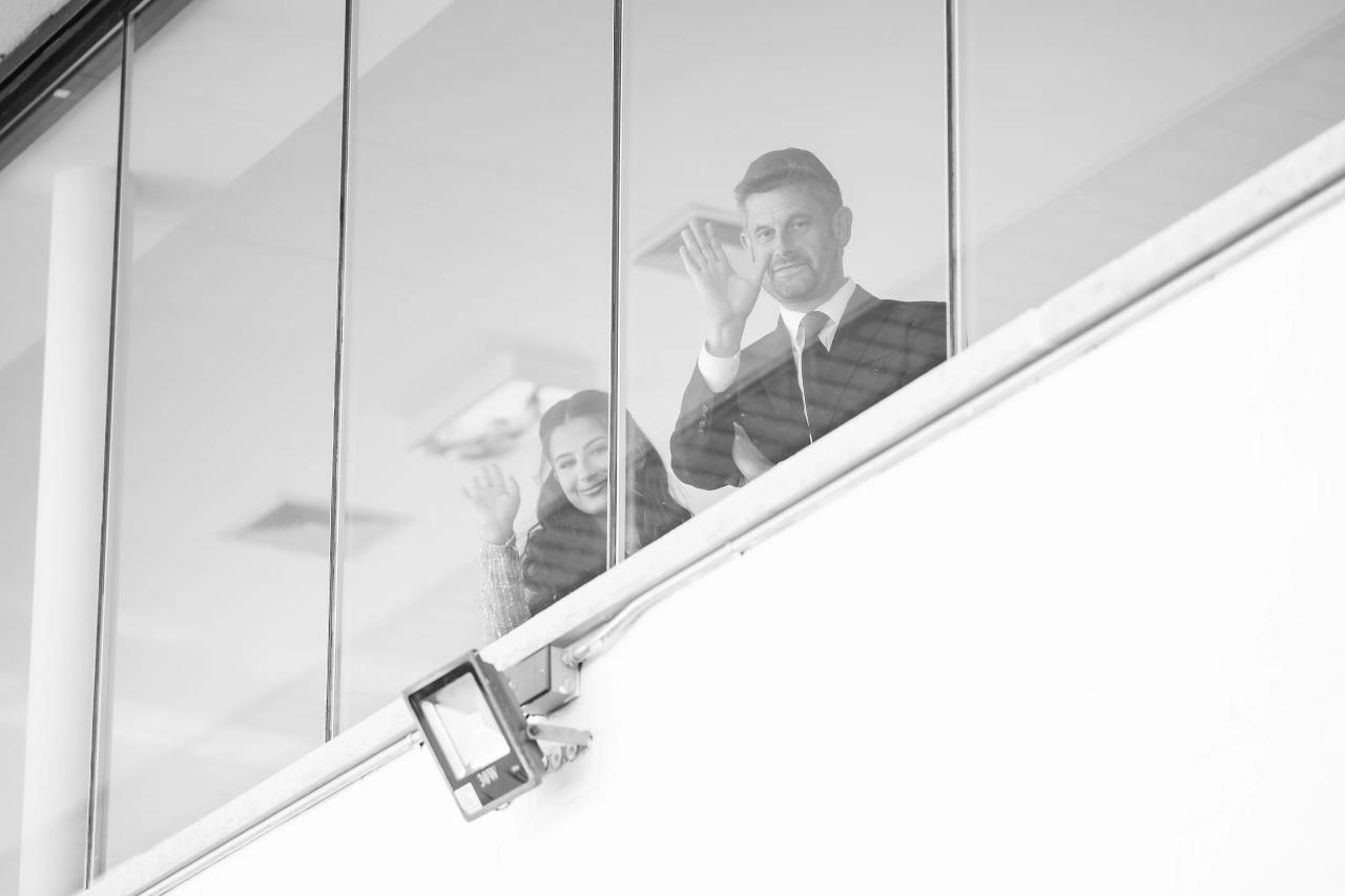 Black-and-white family moment with a man and the bride seen through a reflective glass panel and diagonal stair rails. Wedding photography at Riverview Ballroom, Cliffside Park, NJ.