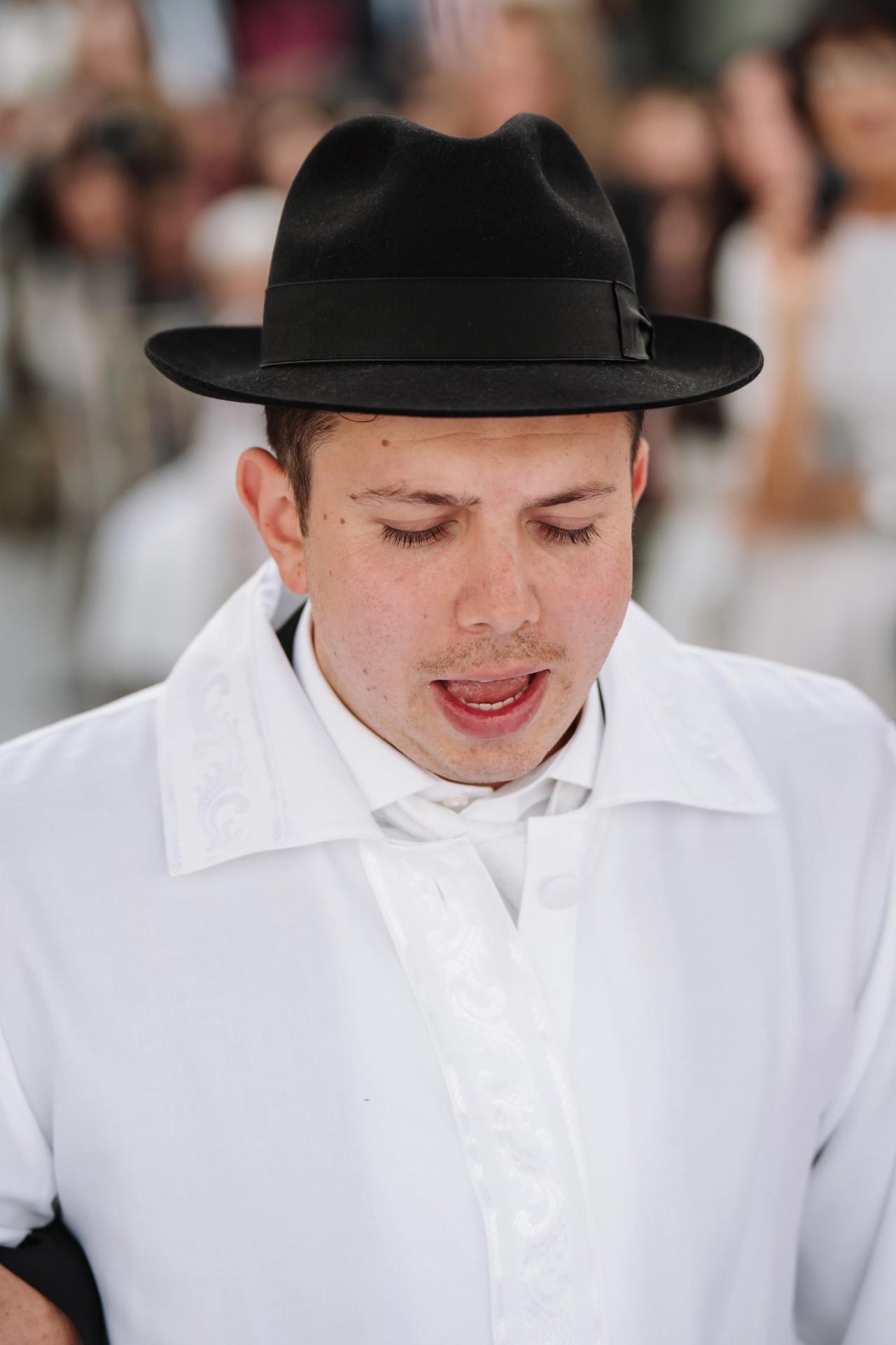 Close-up of a groom in a black hat and white outfit with eyes closed, showing an emotional moment during the celebration. Wedding photography at Riverview Ballroom, Cliffside Park, NJ.