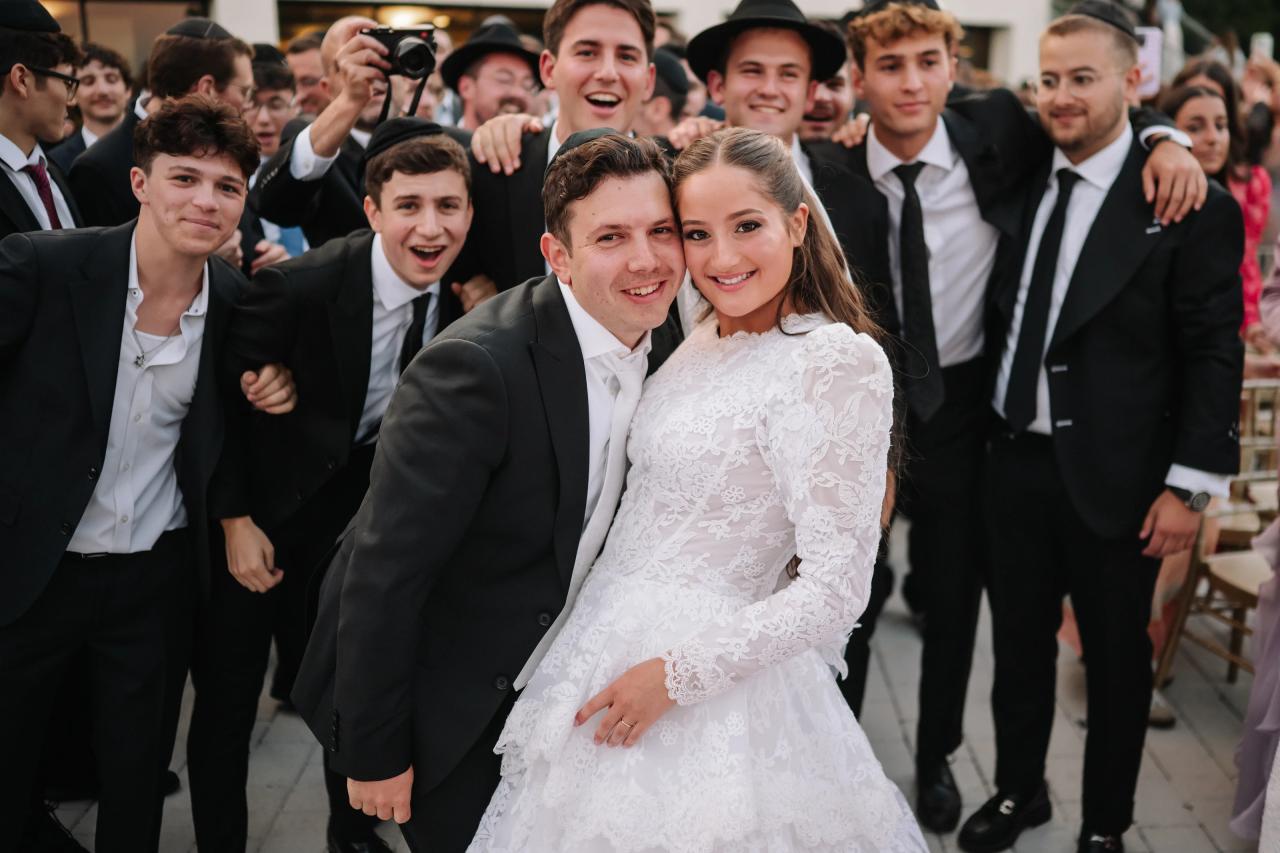 The newlyweds smiling together as friends cheer around them after their wedding ceremony. Wedding photography at Riverview Ballroom, Cliffside Park, NJ.