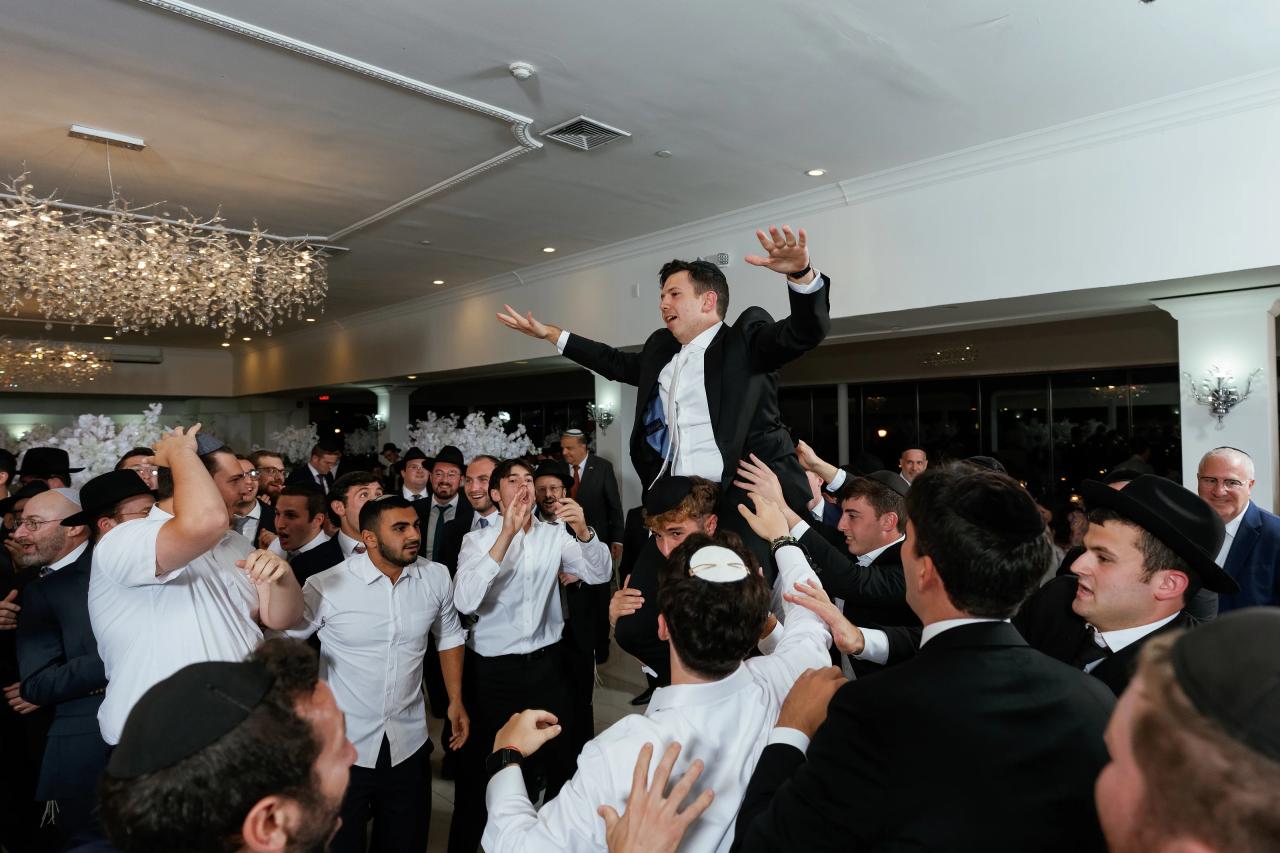 The groom hoisted above the wedding dance floor, smiling with both arms outstretched. Wedding photography at Riverview Ballroom, Cliffside Park, NJ.