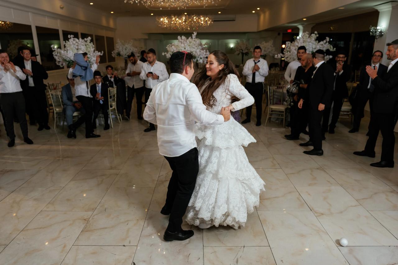 The newlyweds dance together as the bride’s dress sweeps outward and guests watch beyond. Wedding photography at Riverview Ballroom, Cliffside Park, NJ.