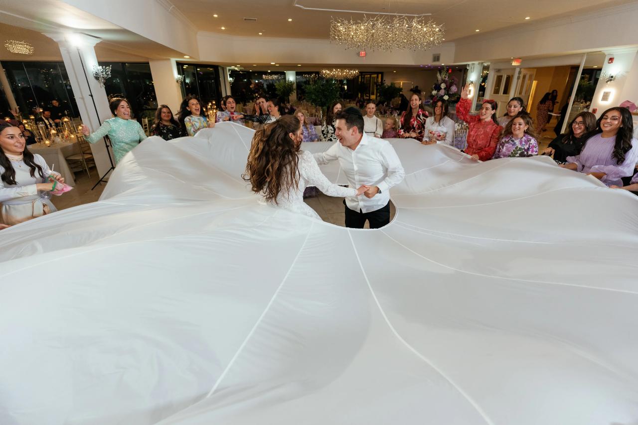 The newlyweds celebrating beneath a billowing white parachute on the wedding dance floor. Wedding photography at Riverview Ballroom, Cliffside Park, NJ.