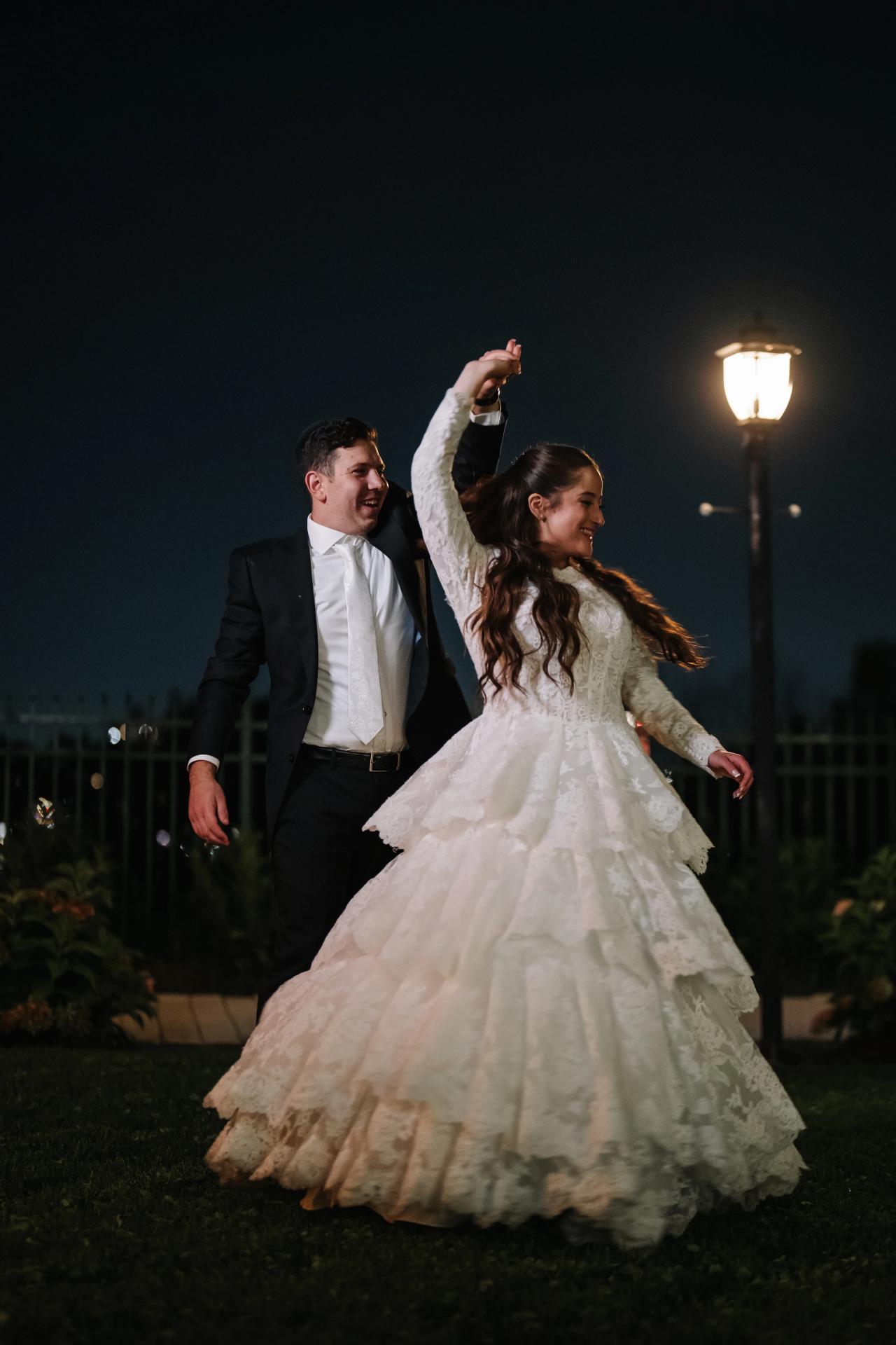 The bride twirls beneath a garden lamp, her wedding dress sweeping across the night portrait. Wedding photography at Riverview Ballroom, Cliffside Park, NJ.