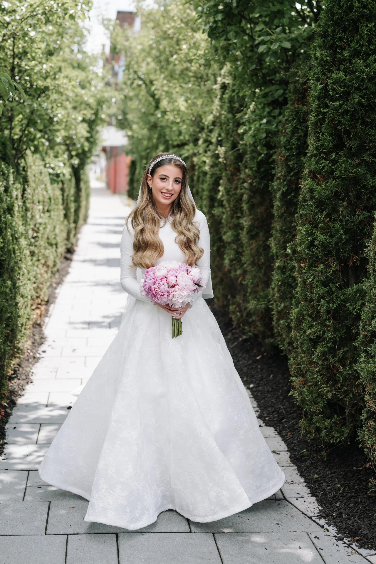 Bride with her bouquet framed by soft greenery in a hedge-lined passage. Wedding photography at Brightstone, Passaic, NJ.