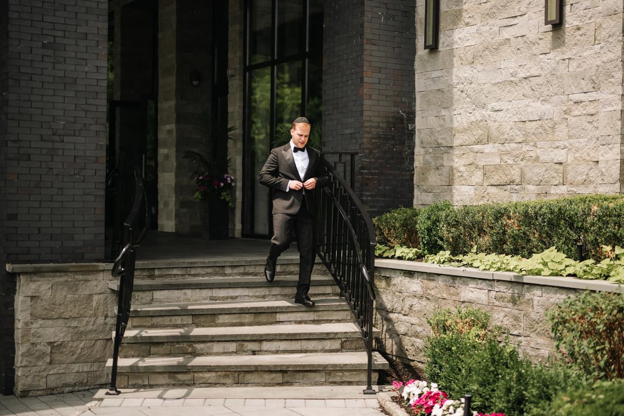Groom on the entrance steps framed by iron railings. Wedding photography at Brightstone, Passaic, NJ.