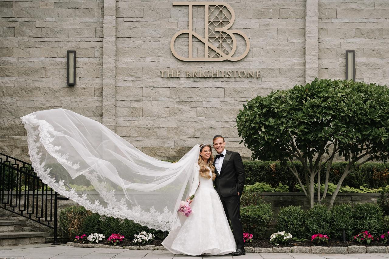 A sweeping lace veil frames the bride and groom beneath The Brightstone Hall facade in Passaic, NJ. Wedding photography.