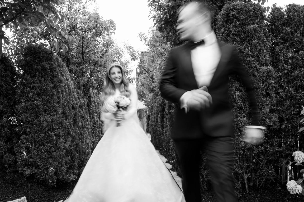 Intentional black-and-white motion blur as the groom passes in front of the bride in a hedge-lined passage. Wedding photography at Brightstone, Passaic, NJ.