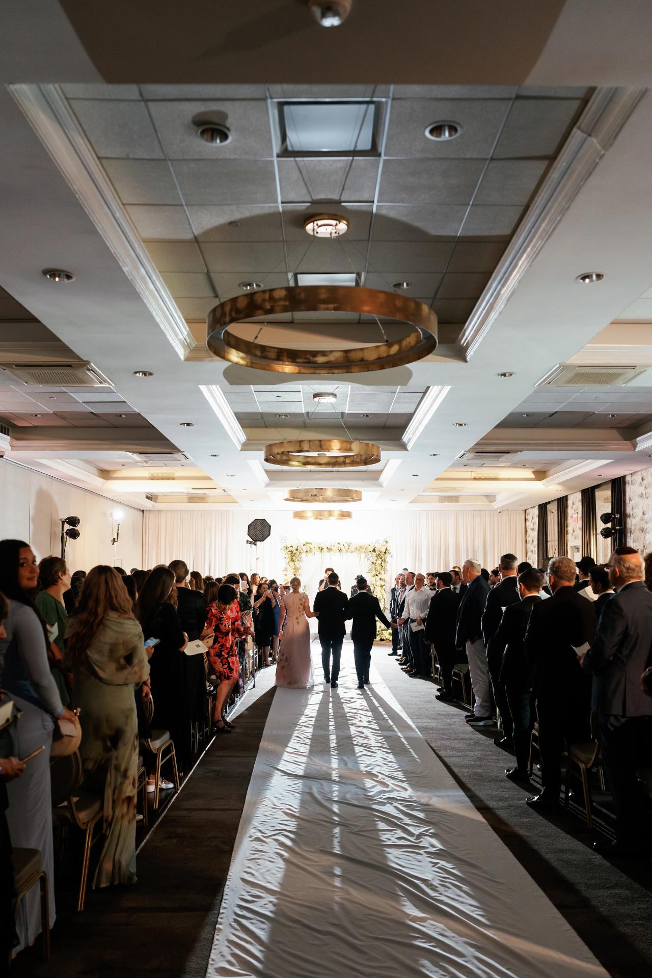 Guests line a long ceremony aisle crossed by geometric light. Wedding photography at Brightstone, Passaic, NJ.