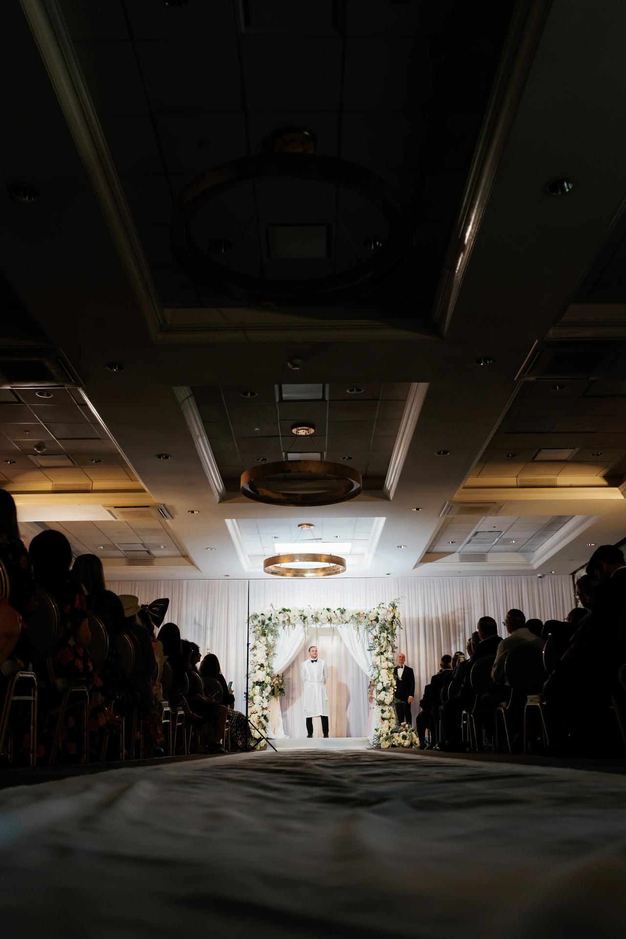 Low architectural view toward the white floral chuppah. Wedding photography at Brightstone, Passaic, NJ.