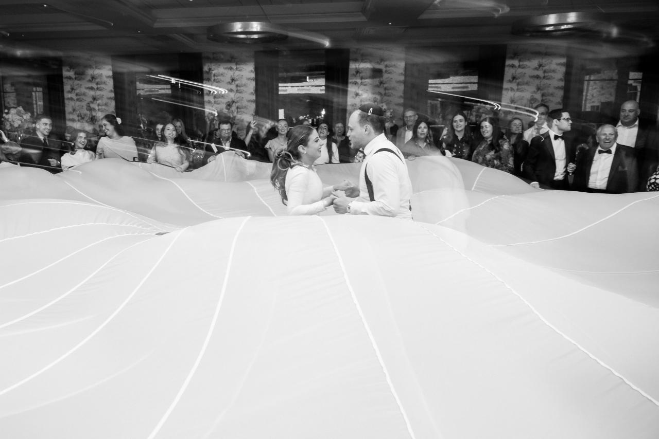 Black-and-white flash trails surround the couple beneath a billowing white parachute. Wedding photography at Brightstone, Passaic, NJ.