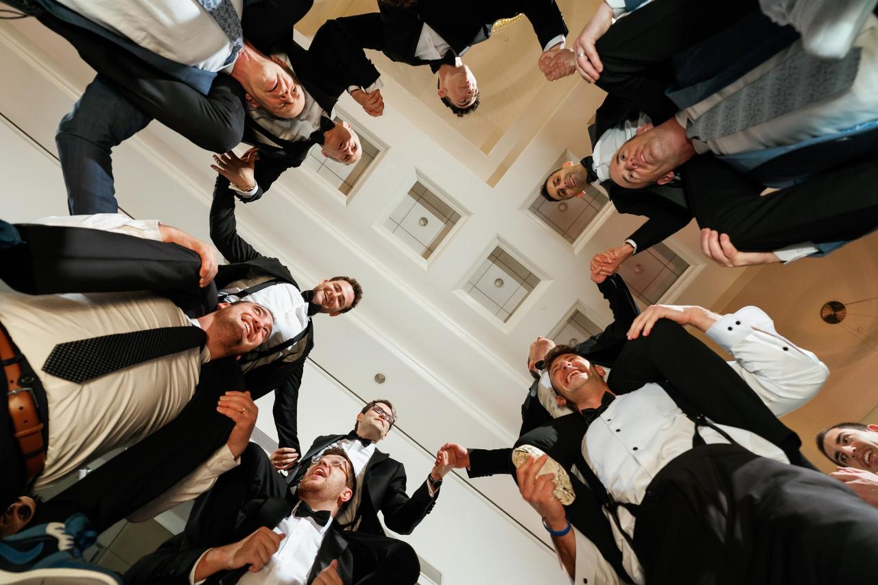 A low angle looks up into a circle of celebrating men. Wedding photography at Brightstone, Passaic, NJ.