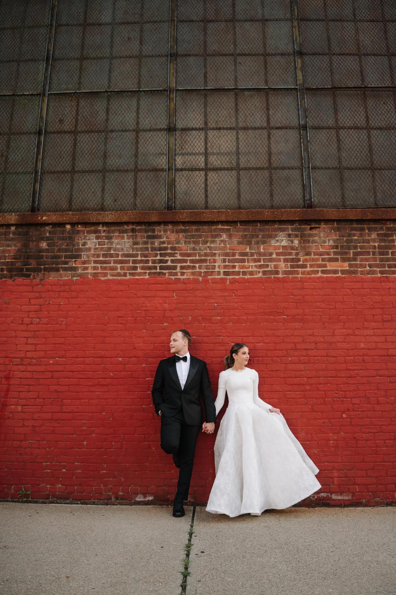 From this Brightstone Hall wedding: full-length couple portrait beneath a tall industrial window against geometric red brick. Wedding photography.