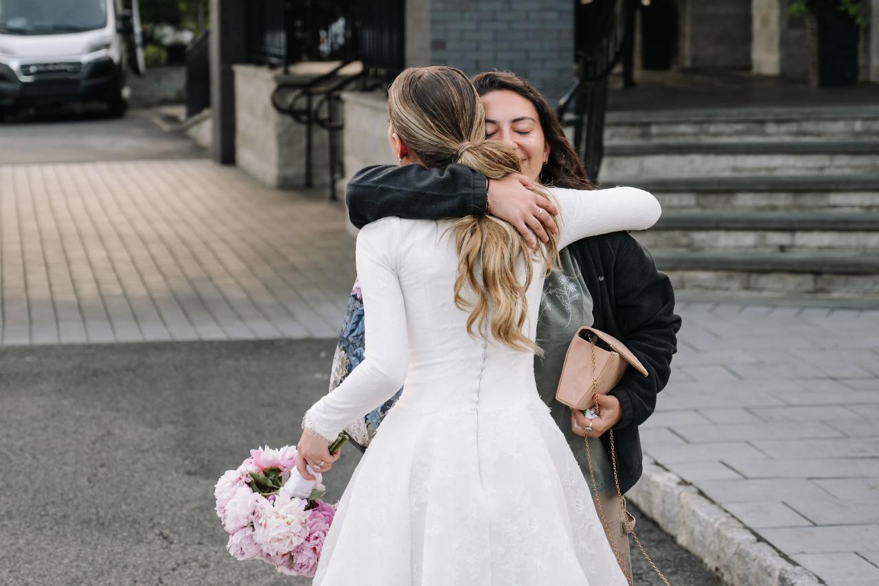 The bride closes her eyes while embracing a guest outside the entrance. Wedding photography at Brightstone, Passaic, NJ.