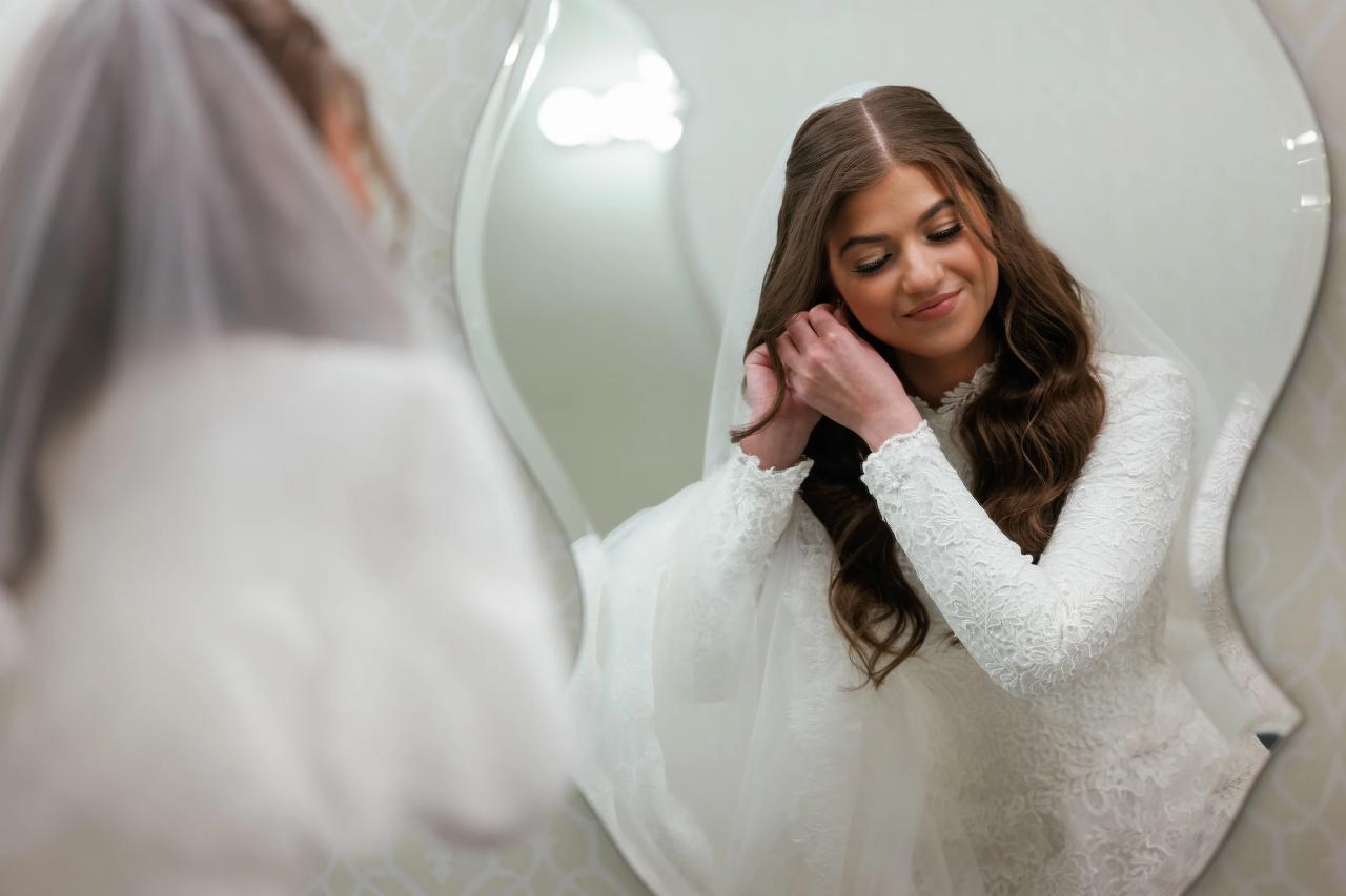 Bride reflected in oval mirror while fastening an earring. Wedding photography at The Palace, Brooklyn, NY.