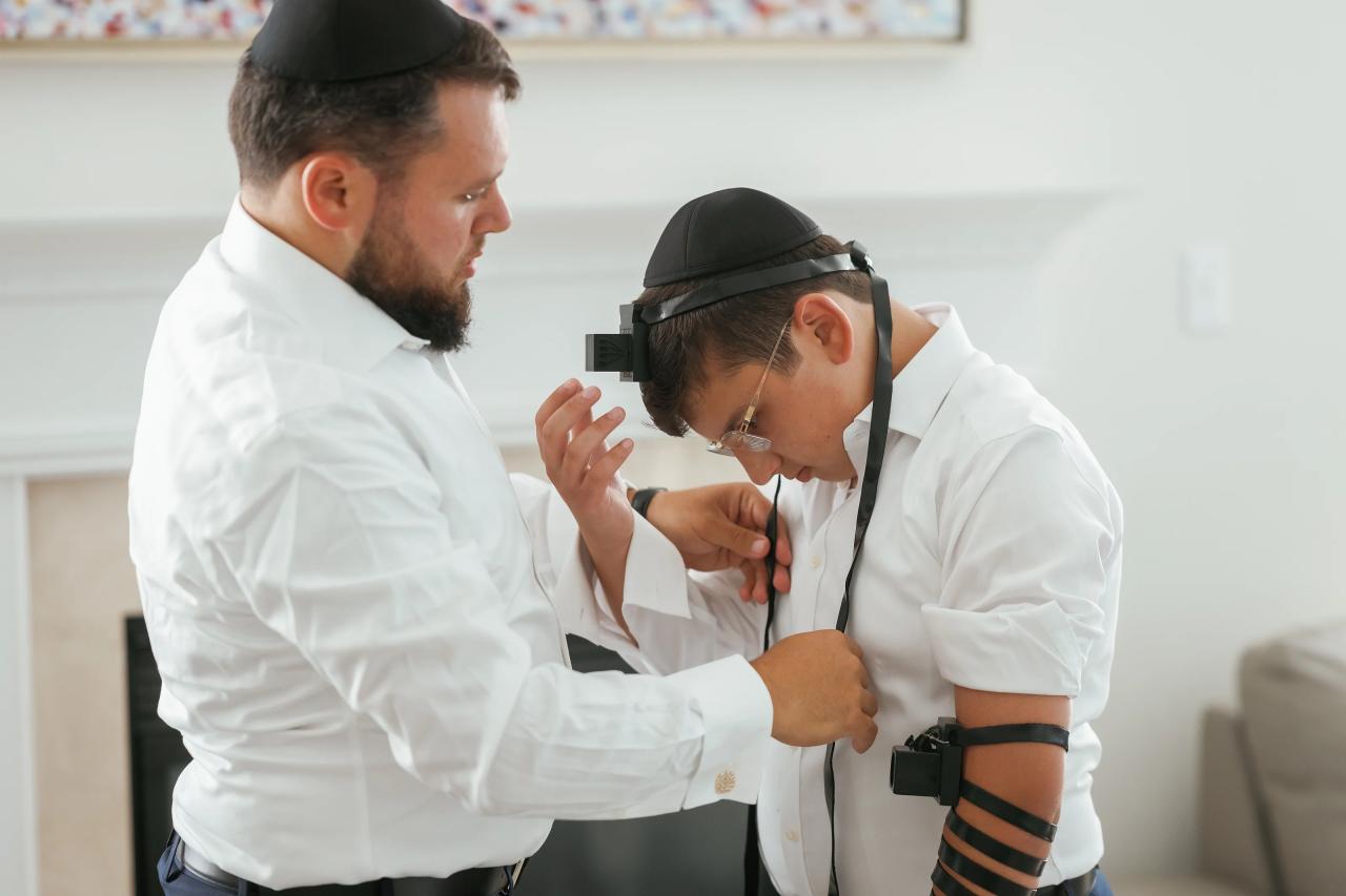 A father kisses his son during tefillin preparation, before the Eagle Ridge bar mitzvah. Bar Mitzvah photography.