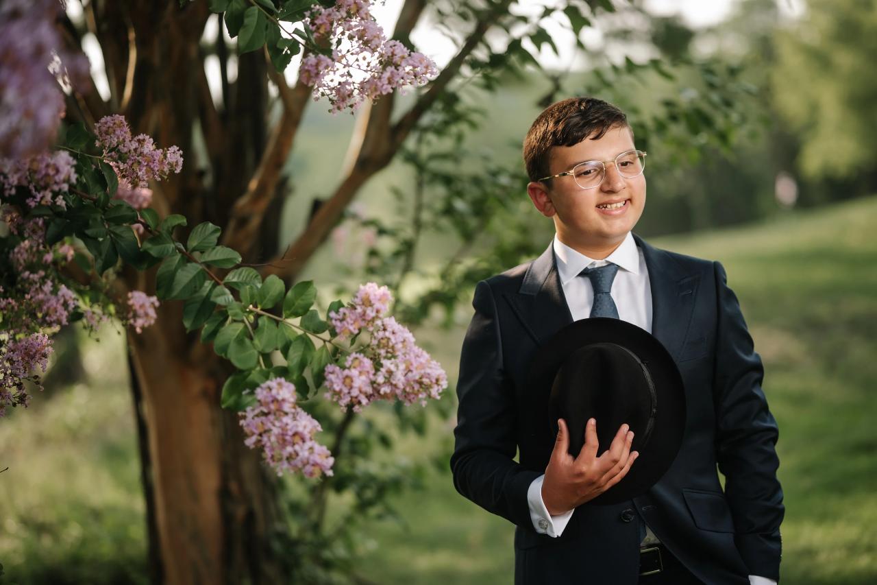 The celebrant holds his hat beneath flowering branches. Bar Mitzvah photography at Eagle Ridge, Lakewood, NJ.