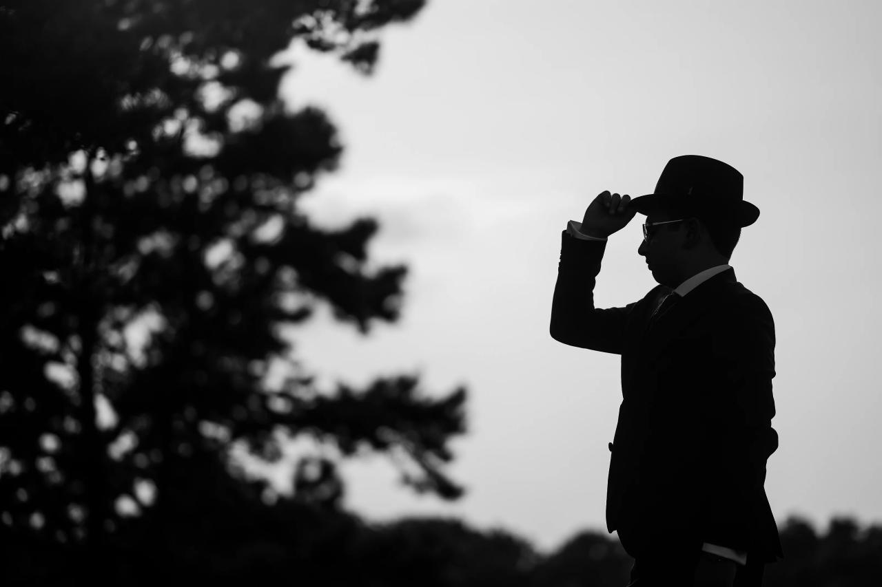 A monochrome silhouette of the celebrant lifting his hat against a bright sky. Bar Mitzvah photography at Eagle Ridge, Lakewood, NJ.