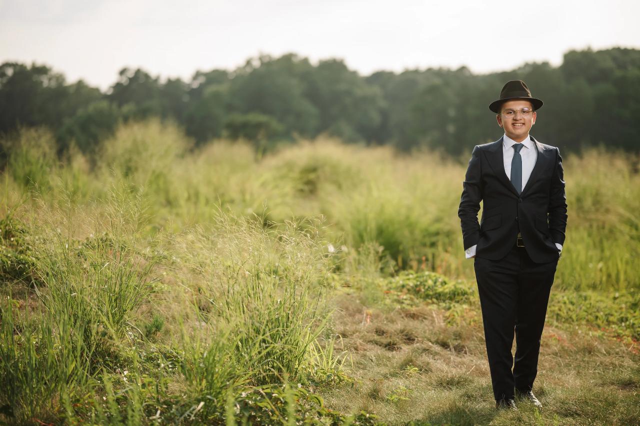 The bar mitzvah boy stands among tall grasses in warm outdoor light. Bar Mitzvah photography at Eagle Ridge, Lakewood, NJ.