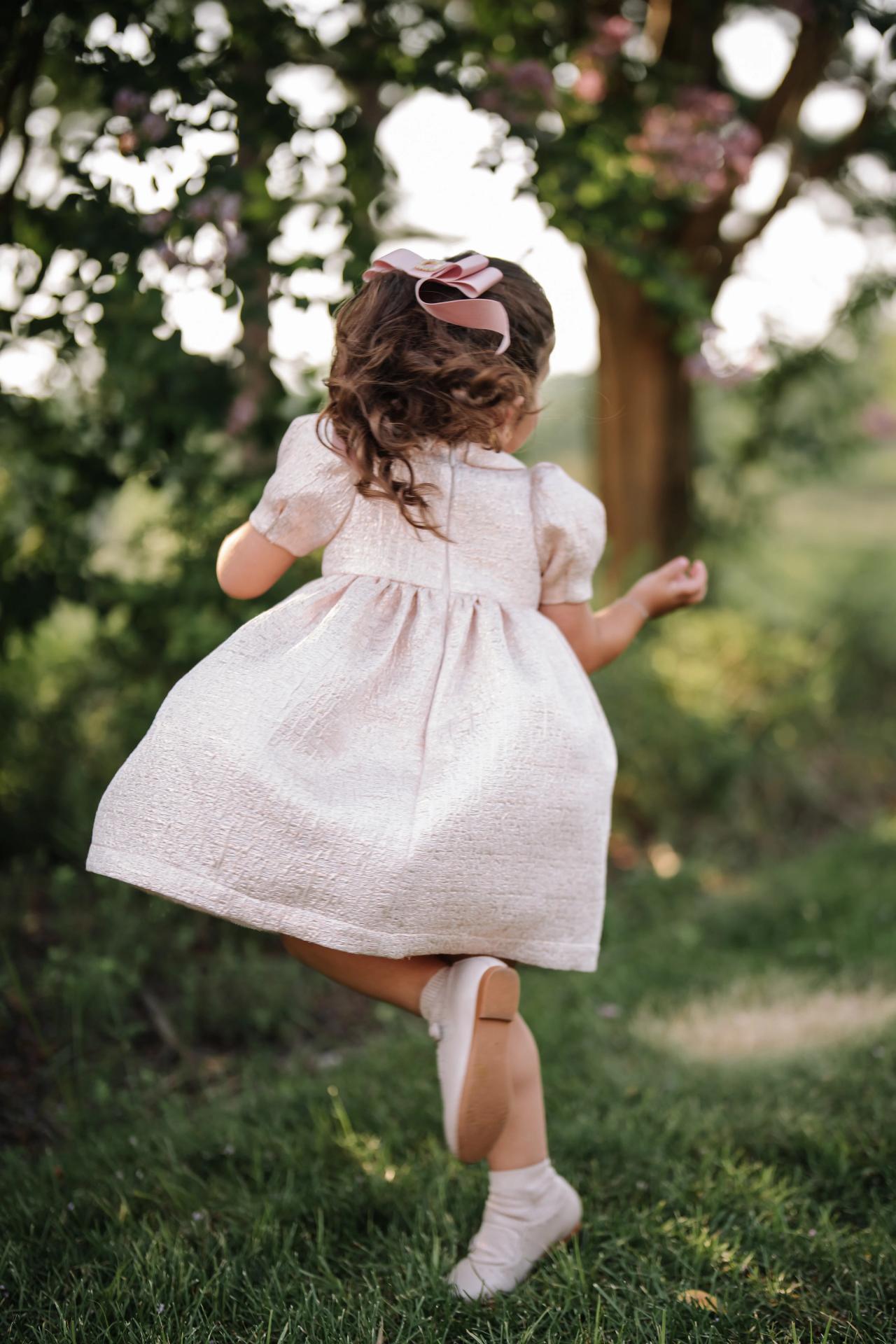 A child twirls in a pink dress beneath the trees. Bar Mitzvah photography at Eagle Ridge, Lakewood, NJ.