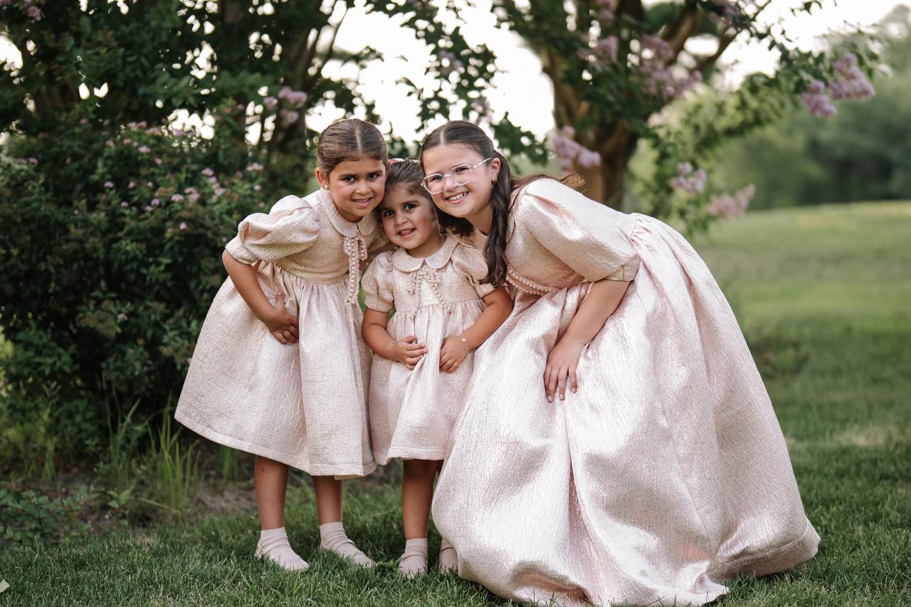 Three sisters lean closely together and laugh in the garden. Bar Mitzvah photography at Eagle Ridge, Lakewood, NJ.