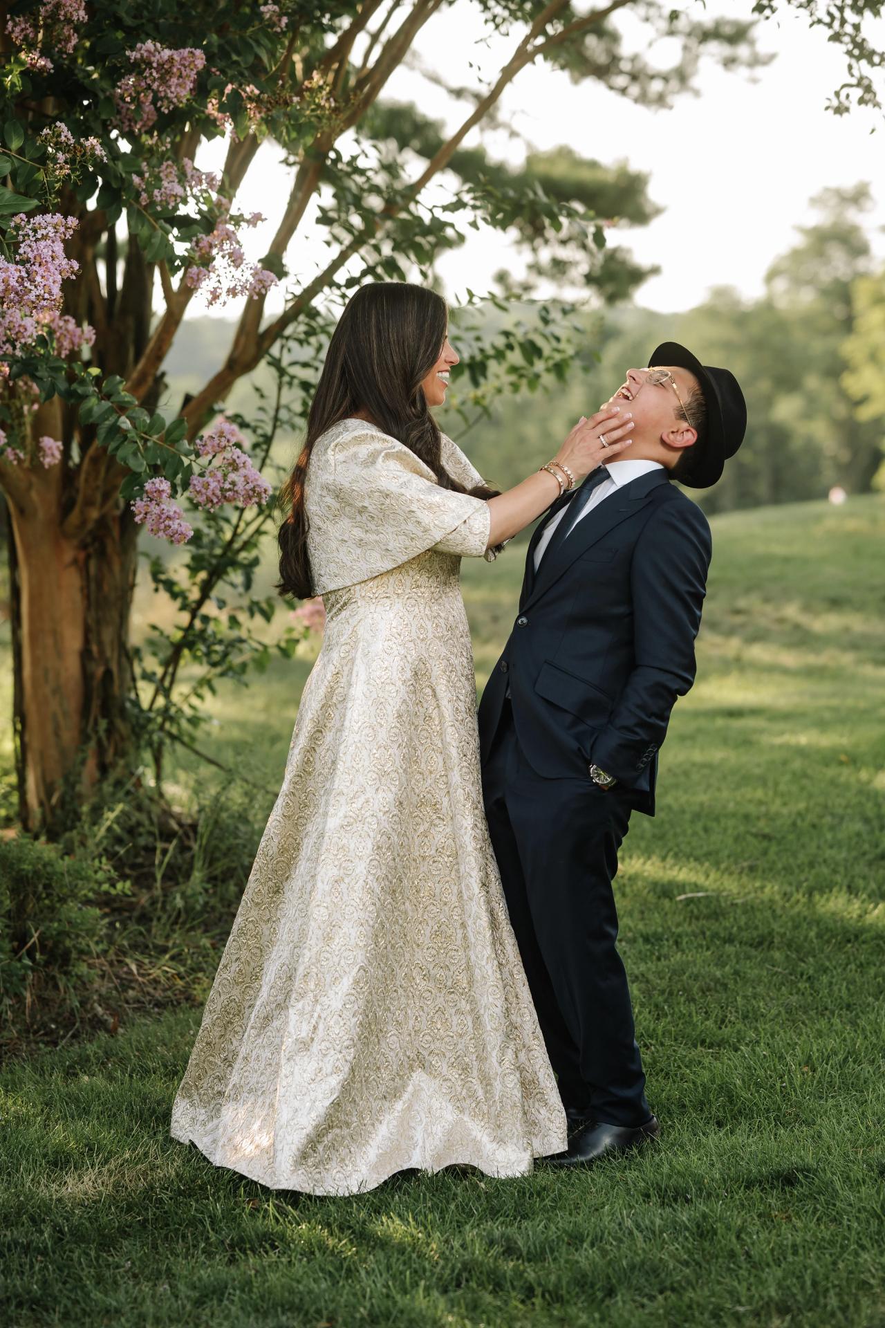 A mother kisses her son beneath flowering trees. Bar Mitzvah photography at Eagle Ridge, Lakewood, NJ.