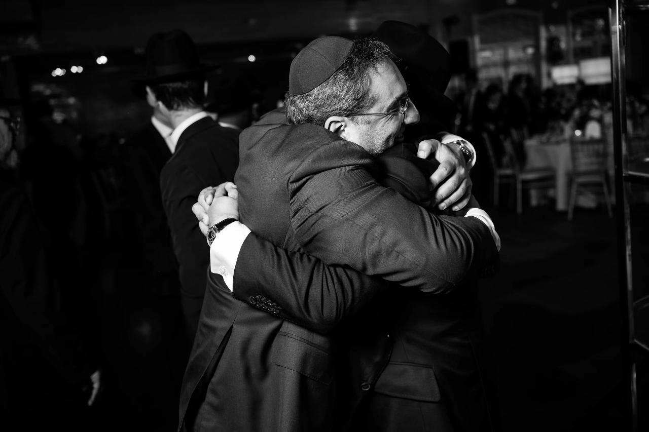 Guests embrace in a black-and-white reception photograph. Bar Mitzvah photography at Eagle Ridge, Lakewood, NJ.