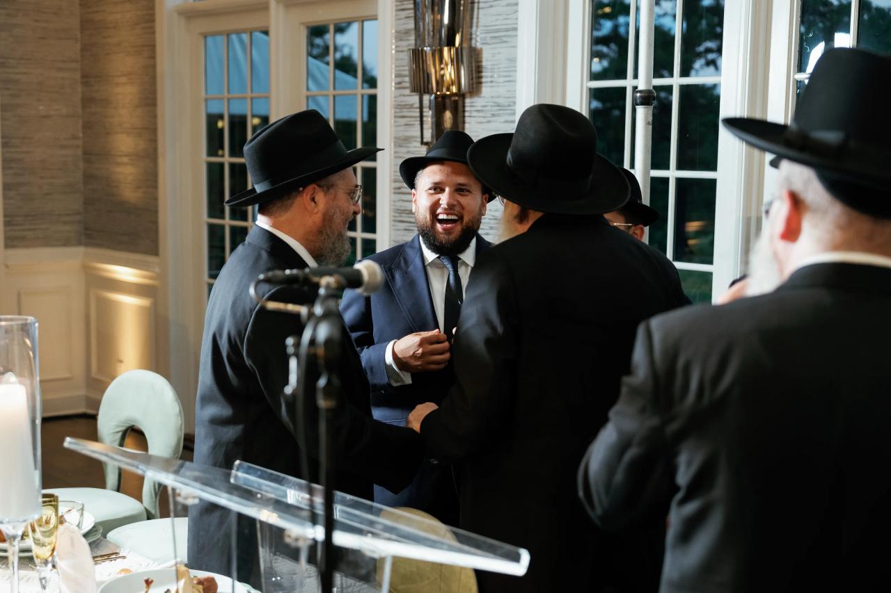 Guests share an expressive greeting beside a foreground microphone. Bar Mitzvah photography at Eagle Ridge, Lakewood, NJ.