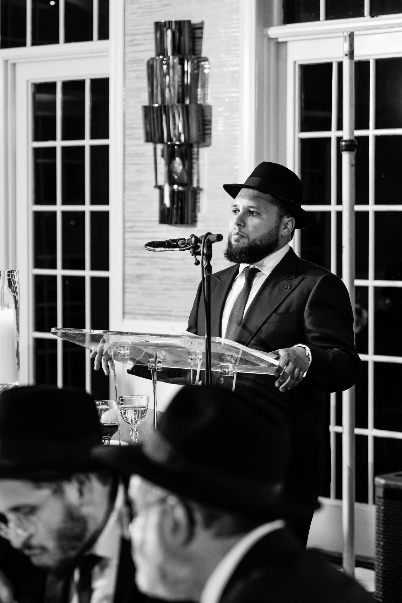 A musician performs in black and white beside tall window grids. Bar Mitzvah photography at Eagle Ridge, Lakewood, NJ.