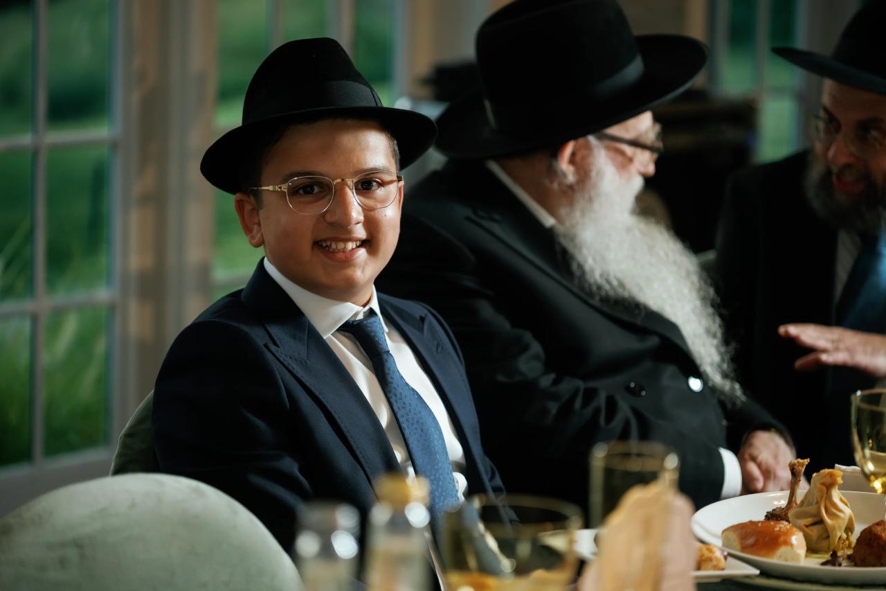 The celebrant smiles beside an elder at a reception table. Bar Mitzvah photography at Eagle Ridge, Lakewood, NJ.