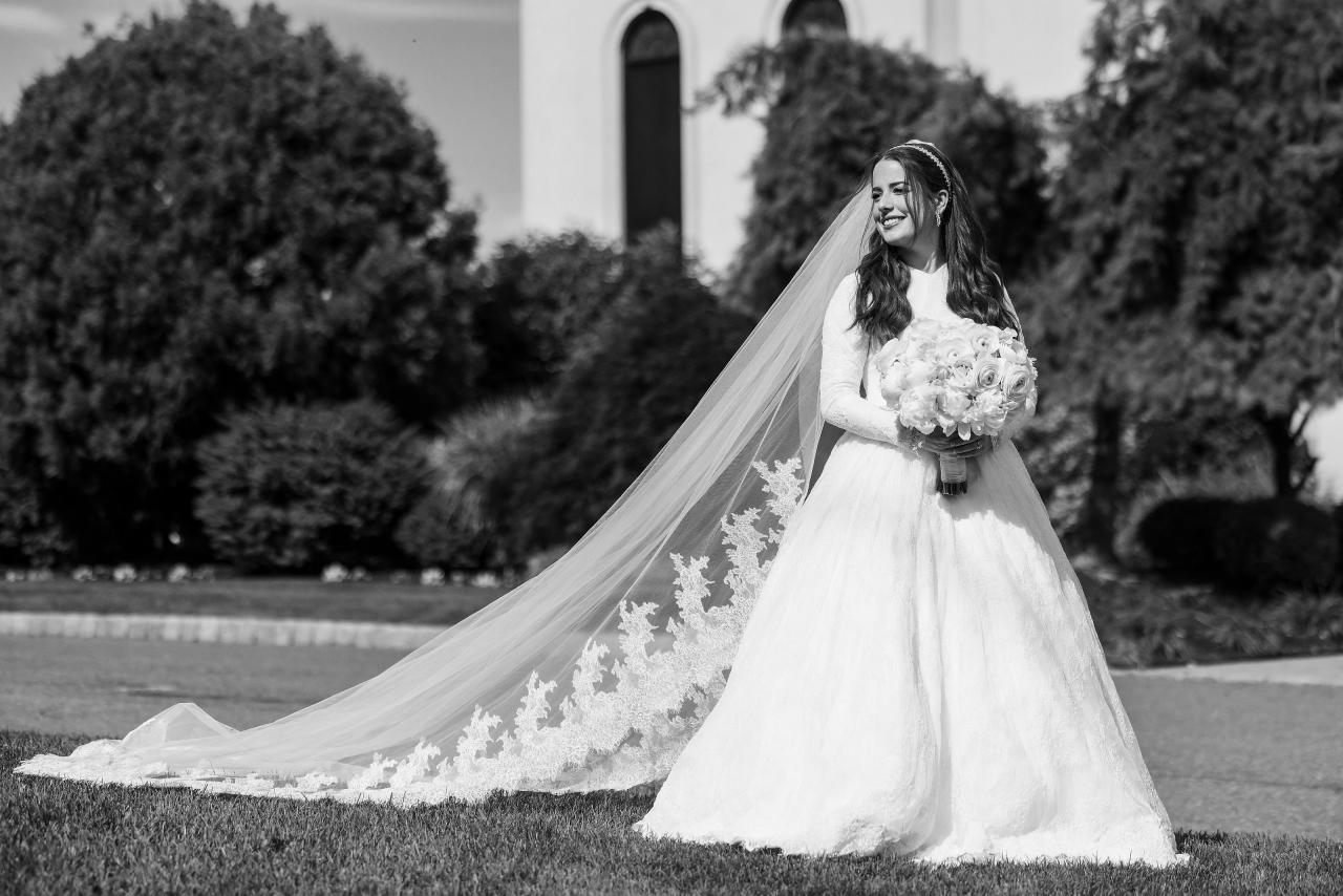 A black-and-white bridal portrait with the veil sweeping outward against garden foliage. Wedding photography at Ateres Charna, New Square, NY.