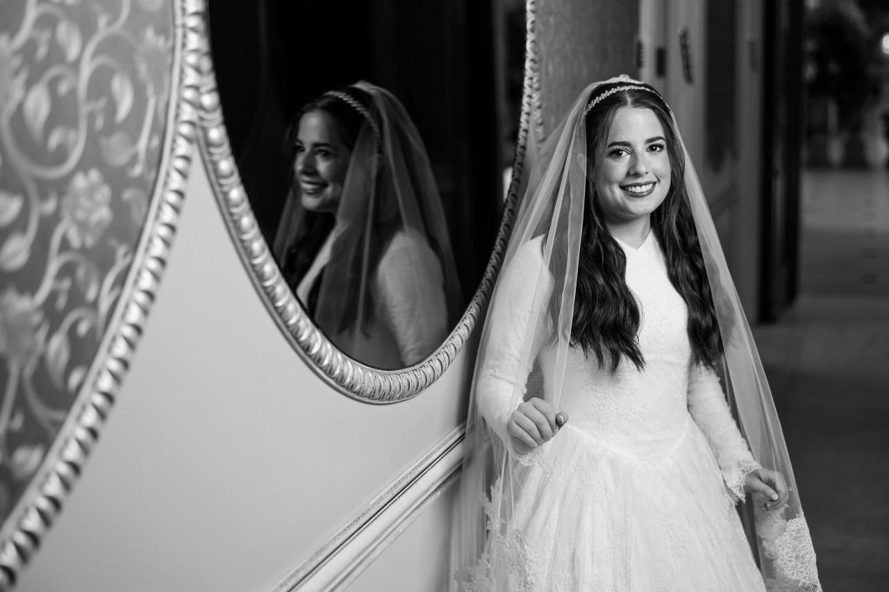 The bride reflected in an ornate oval mirror, photographed in black and white. Wedding photography at Ateres Charna, New Square, NY.