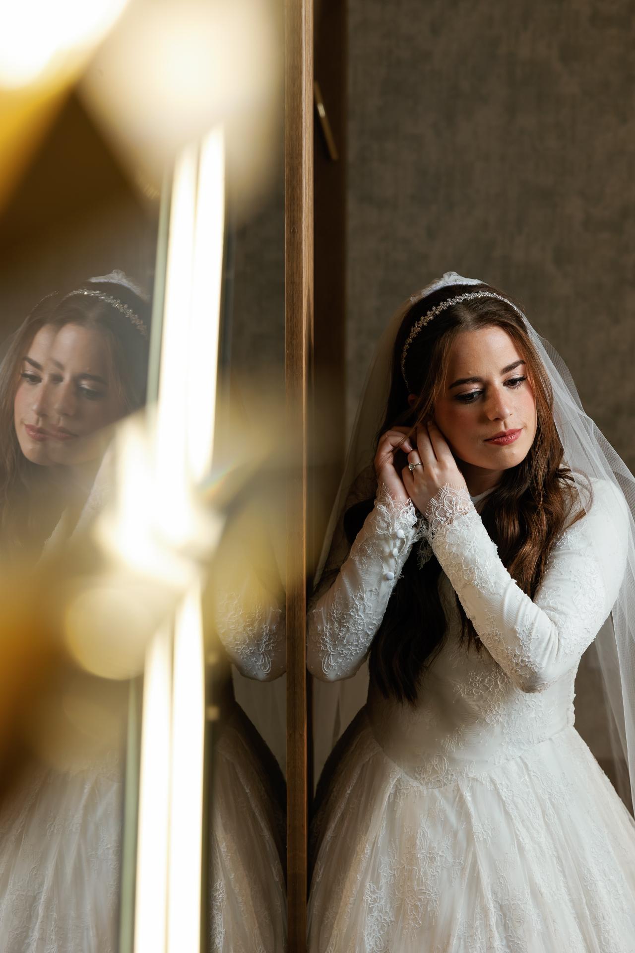 Warm flare and a reflection of the bride’s face in a layered bridal portrait. Wedding photography at Ateres Charna, New Square, NY.