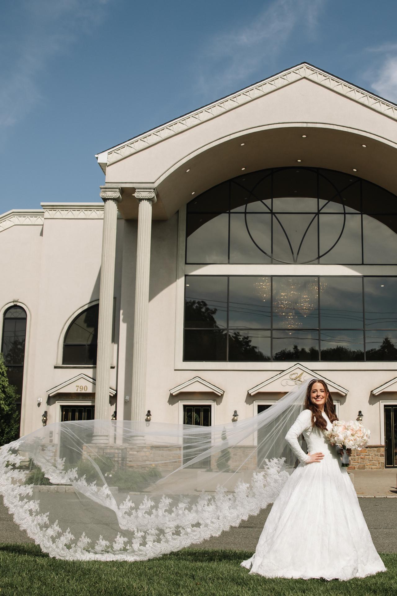 A wide bridal portrait against the tall arched facade of Ateres Charna. Wedding photography.