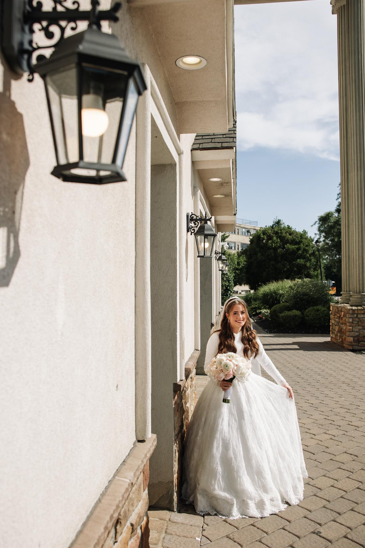 Sunlight through tall windows framing the bride and her full wedding-dress train. Wedding photography at Ateres Charna, New Square, NY.