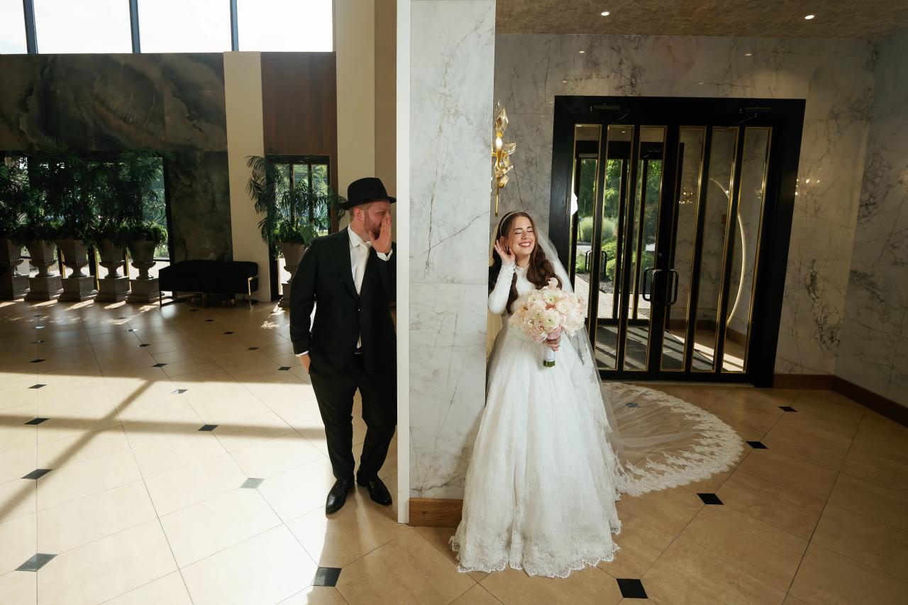 The bride and groom framed separately by entryway columns in a balanced architectural portrait. Wedding photography at Ateres Charna, New Square, NY.