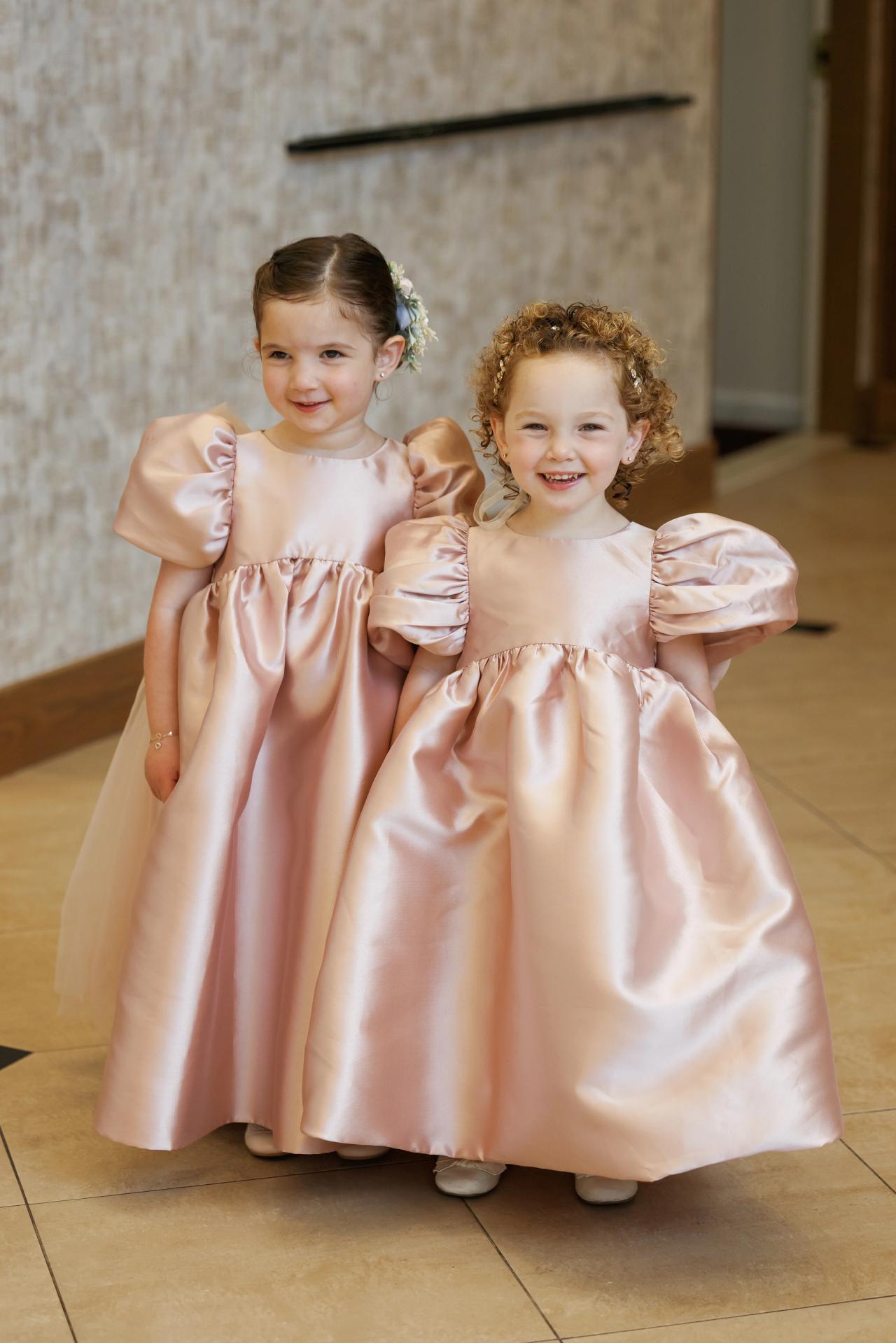 Two children in blush pink dresses sharing a tender affectionate moment. Wedding photography at Ateres Charna, New Square, NY.