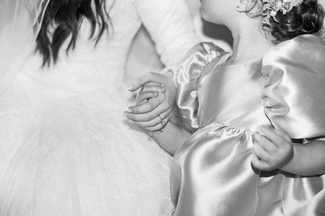 Clasped hands against the bride’s wedding dress during the bedeken, photographed in black and white. Wedding photography at Ateres Charna, New Square, NY.