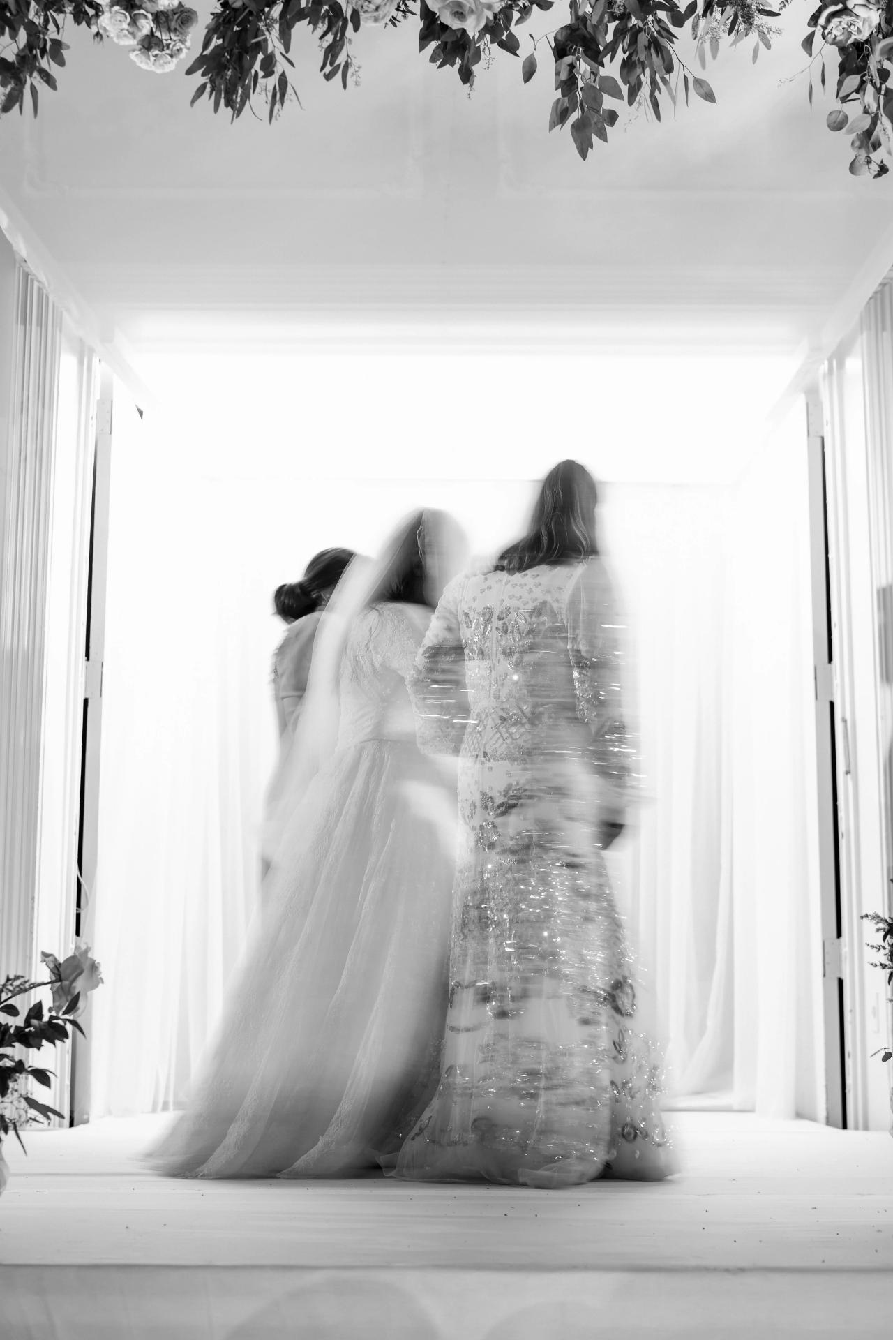 Intentional black-and-white motion blur as the bride circles beneath the indoor chuppah. Wedding photography at Ateres Charna, New Square, NY.