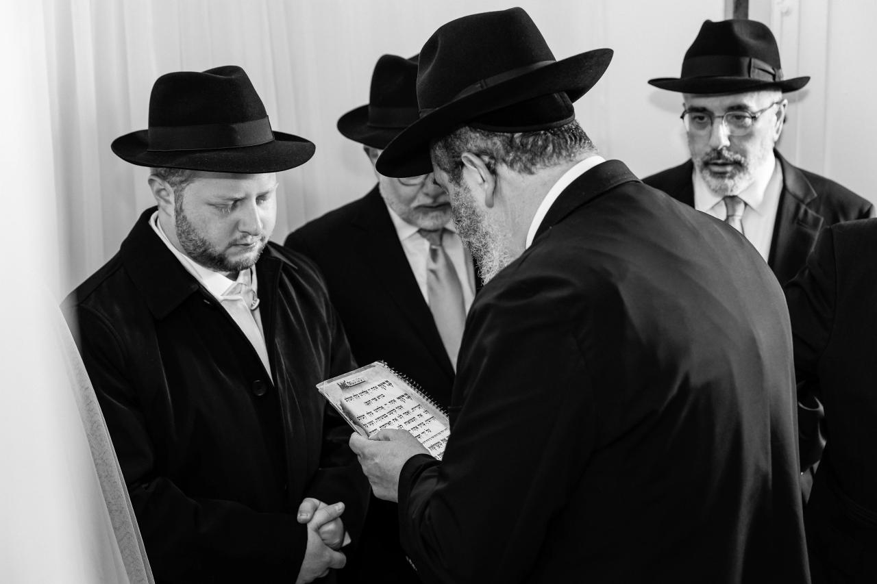 A close black-and-white ceremony portrait of the groom, framed by the bride’s veil and guests. Wedding photography at Ateres Charna, New Square, NY.
