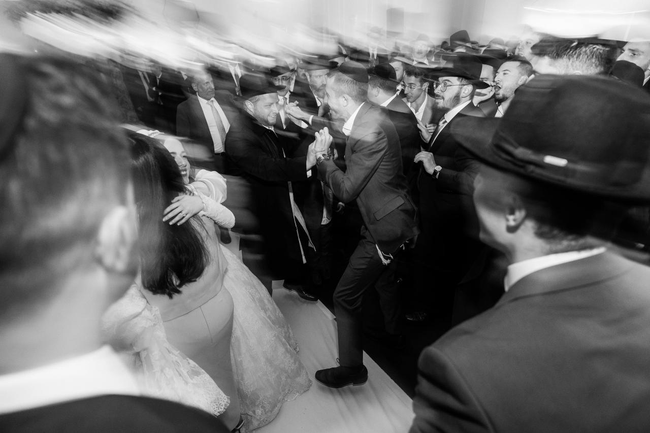 Experimental black-and-white motion blur as the newlyweds move through a celebrating crowd. Wedding photography at Ateres Charna, New Square, NY.