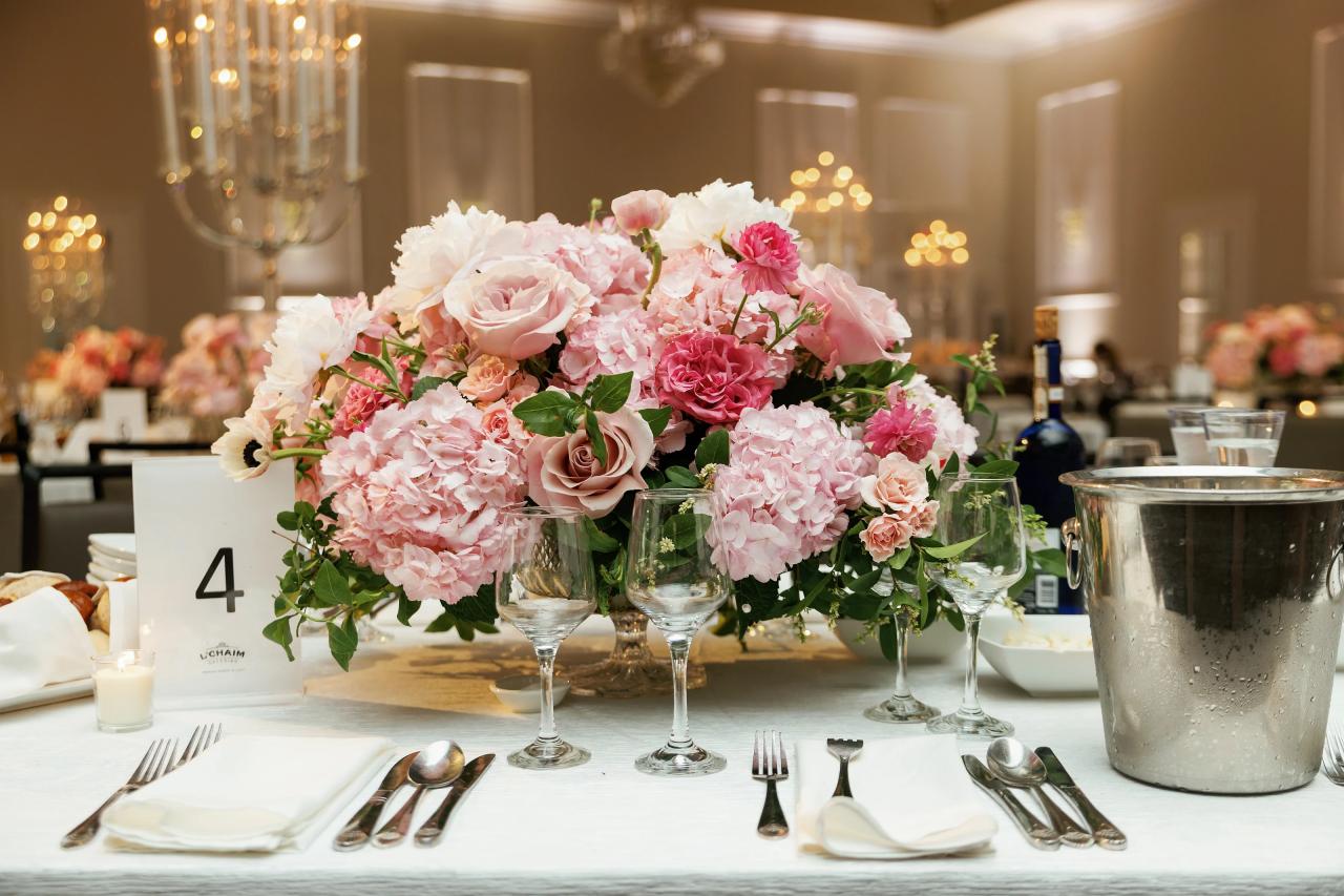 A pink-and-white floral centerpiece with soft candlelight and glass reflections. Wedding photography at Ateres Charna, New Square, NY.