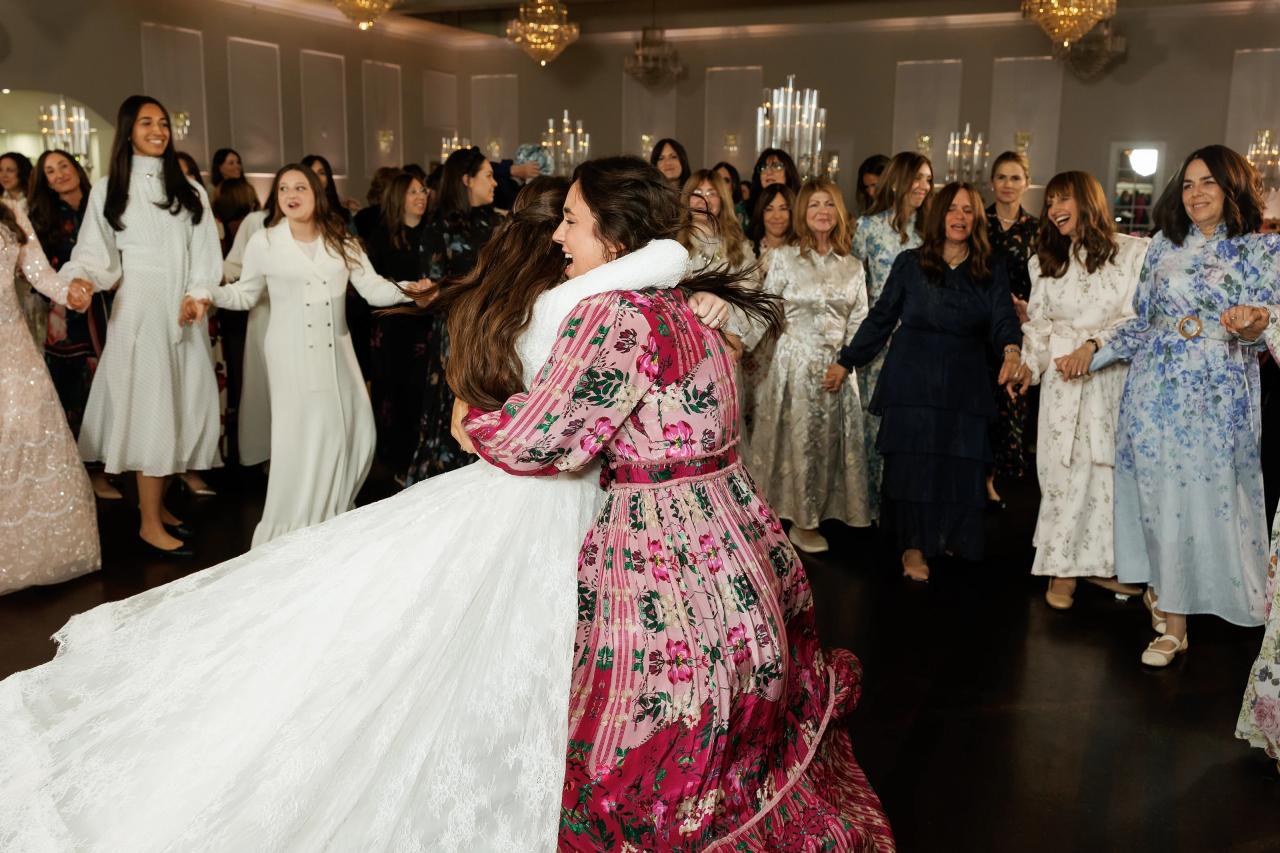 The bride spinning with a guest as her skirt sweeps into a broad white arc. Wedding photography at Ateres Charna, New Square, NY.