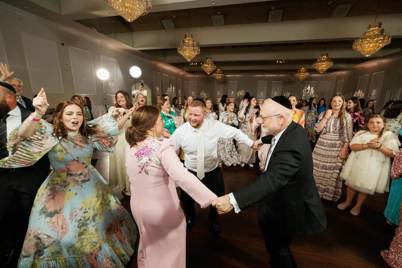 The bride and groom reaching toward each other amid the reception crowd. Wedding photography at Ateres Charna, New Square, NY.
