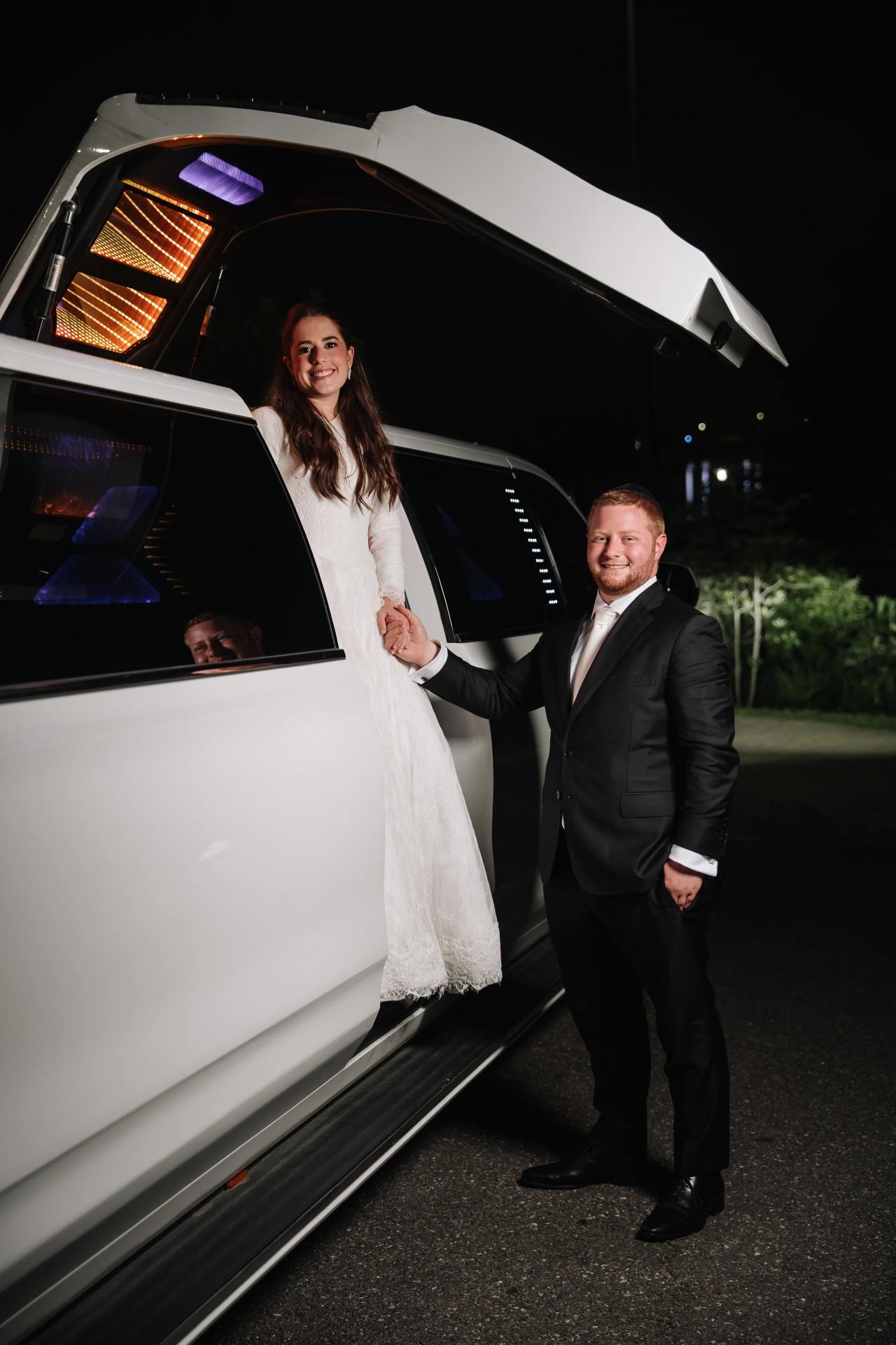 A dramatic night portrait beside a car’s raised door and sculptural lights, from the Ateres Charna wedding portrait collection. Wedding photography.