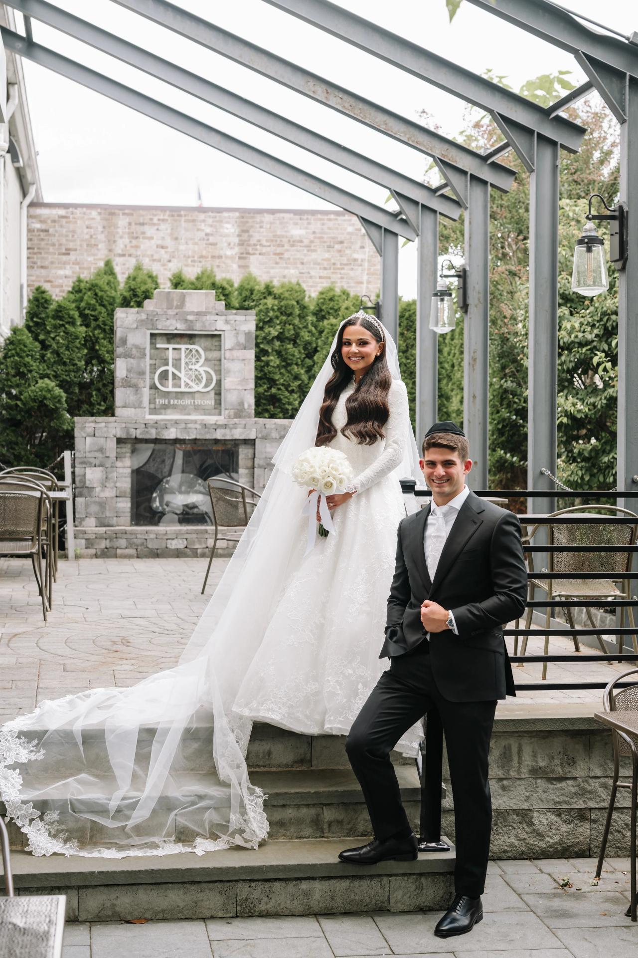 The couple on the entrance steps with railings and a flowing wedding train. Wedding photography at Brightstone, Passaic, NJ.