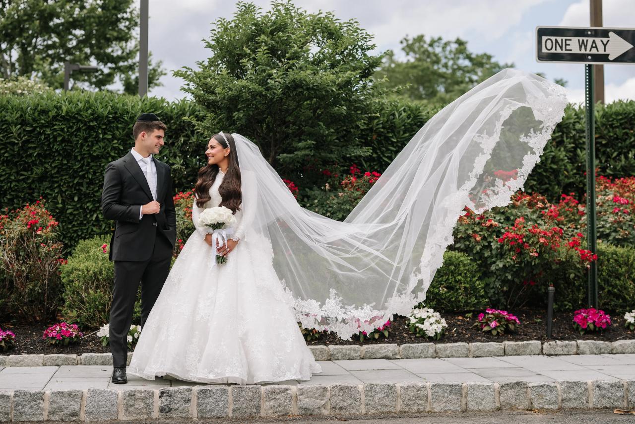 A lace veil forms a long sweeping arc beside the bride and groom outdoors. Wedding photography at Brightstone, Passaic, NJ.